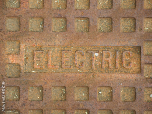 A rusty manhole cover with the word Electric on it, describing what utilities the cover gives access to.