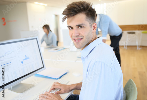 Office worker sitting in front of desktop, colleagues in background
