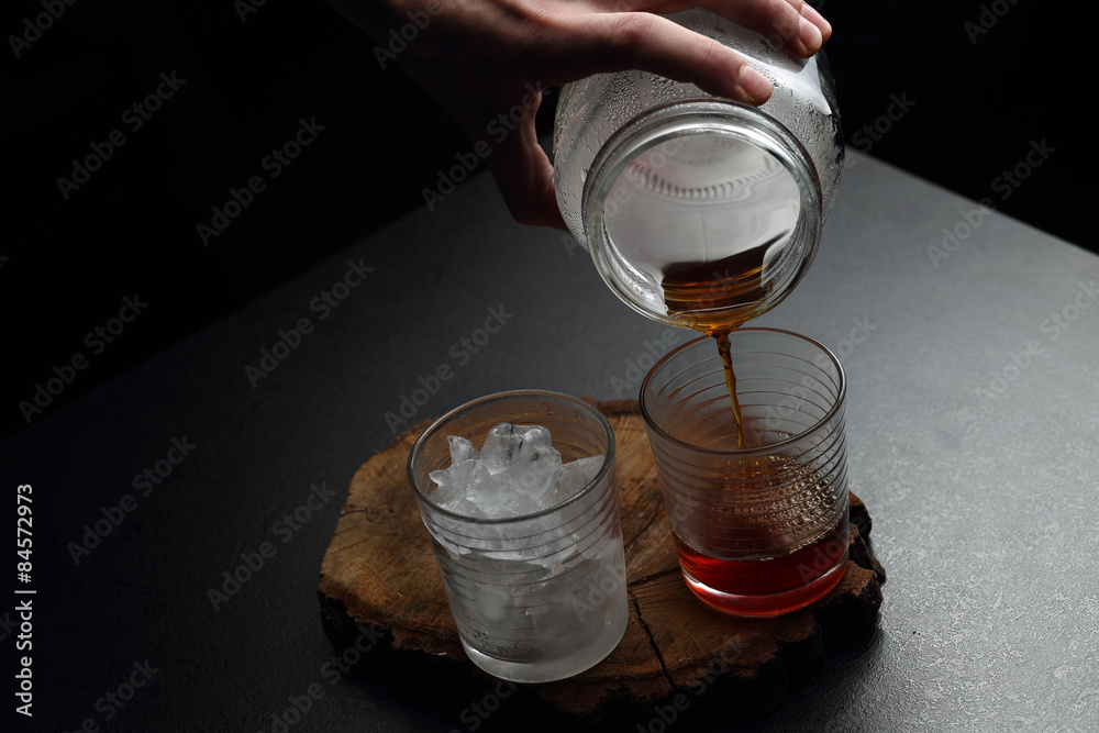 Man`s hand pouring hot and cold coffee into two glasses. Dark ba - obrazy, fototapety, plakaty 