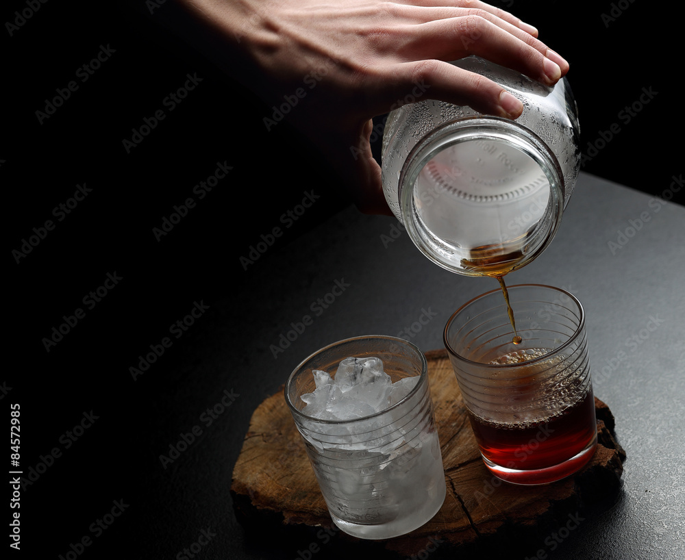 Man`s hand pouring hot and cold coffee into two glasses. Dark ba - obrazy, fototapety, plakaty 