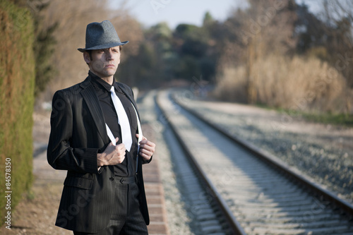 HOMBRE ELEGANTE JUNTO A LAS VIAS DEL TREN CON SOMBRERO Y MALETA photo