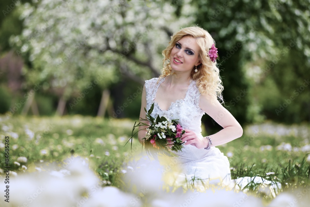 Beautiful young bride in white dress sits field in summer green park