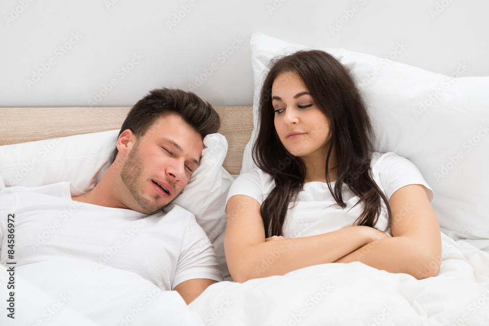 Woman Looking At Man Snoring In Bed At Home Woman Looking At Man Snoring In Bed At Home