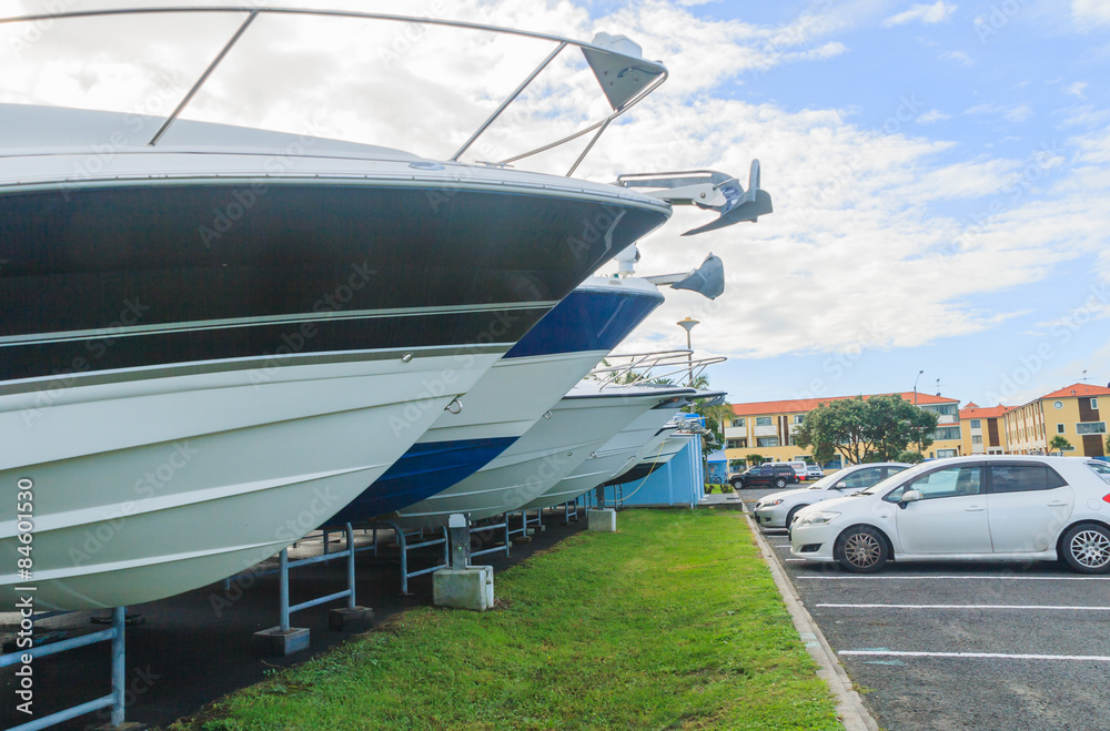 Fototapeta premium The bows of boats sticking out of the rack for storing stand in front of cars