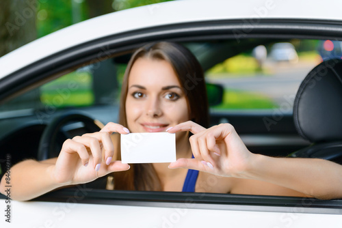 Attractive woman inside car showing card 