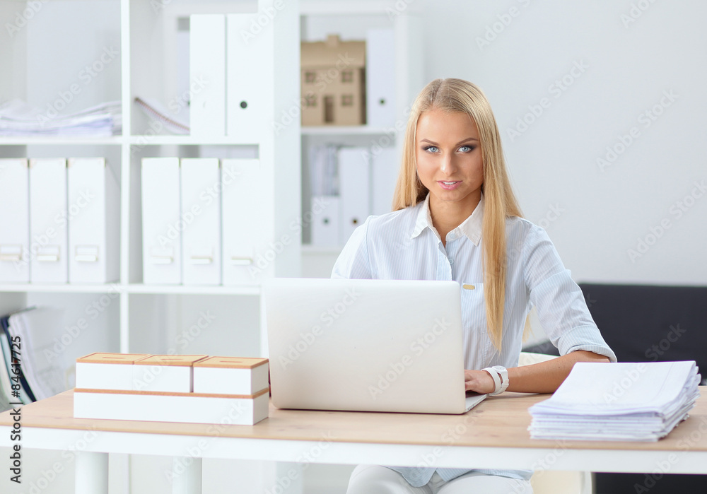 Attractive businesswoman sitting on a desk with laptop in the Attractive businesswoman sitting on a desk with laptop in the