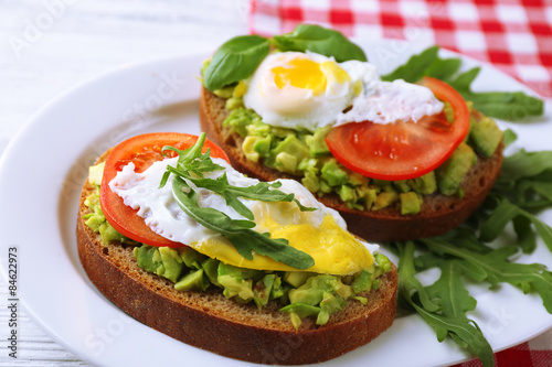 Tasty sandwiches with egg, avocado and vegetables on plate, on wooden background