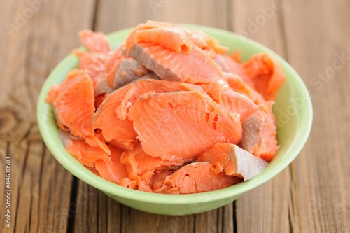 Slices of raw salmon in green bowl on wooden background