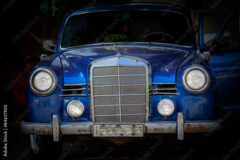 Closeup front view of dark blue old classic vintage car against dark background