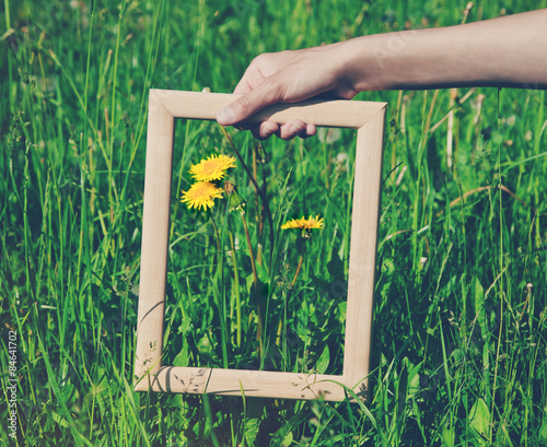 Fototapeta Naklejka Na Ścianę i Meble -  Hand holding a wooden frame on flower background. Care, safety,