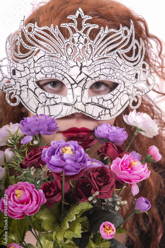Close up view of a mysterious young girl with a white mask and bouquet of flowers.