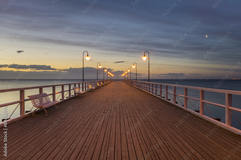 Fototapeta premium drewniane molo nad morzem oświetlone w nocy stylowymi lampami