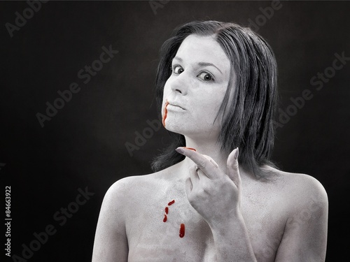 Kobieta smakująca krew pomalowana na biało na ciemnym tle