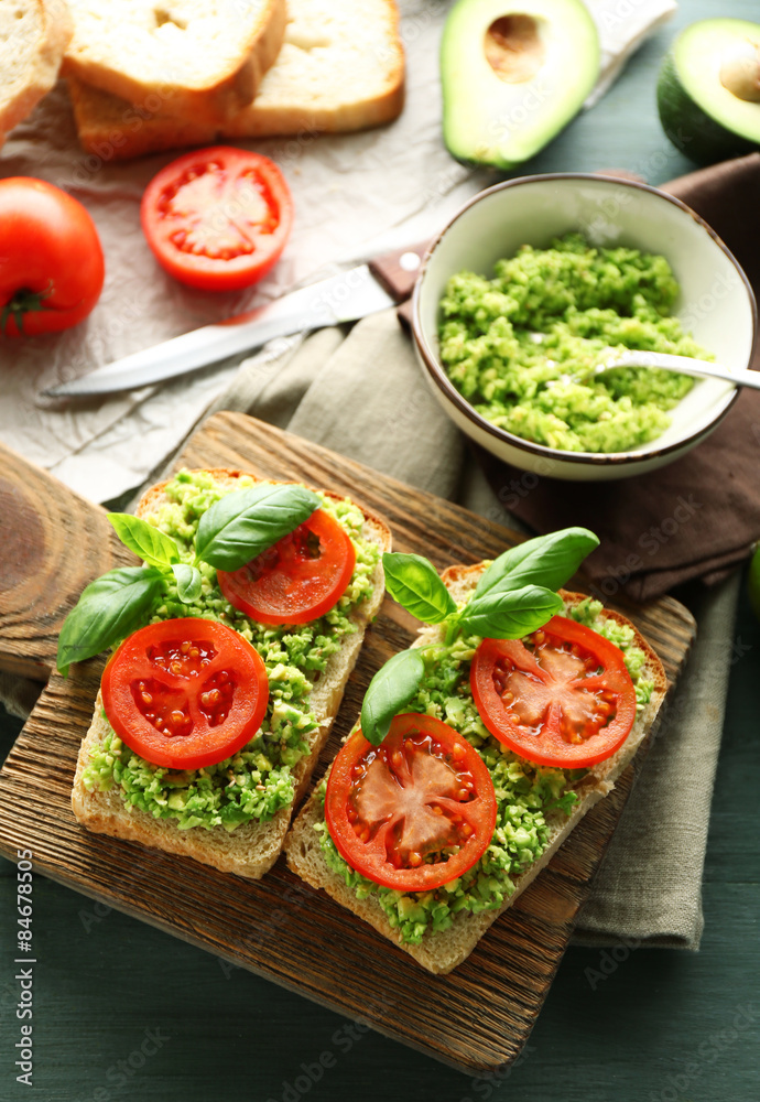 Vegan sandwich with avocado and vegetables on cutting board, on wooden background Vegan sandwich with avocado and vegetables on cutting board, on wooden background