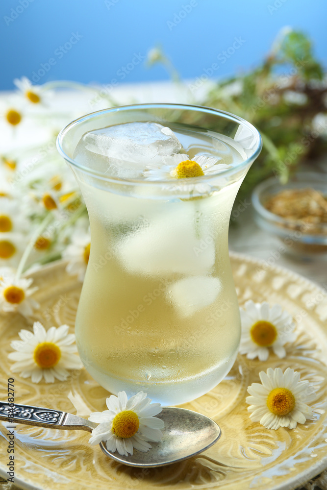 Glass of cold chamomile tea with ice cubes and chamomile flowers on table, on colorful background Glass of cold chamomile tea with ice cubes and chamomile flowers on table, on colorful background