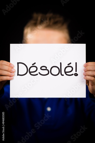 Child holding sign with French word Desole - Sorry