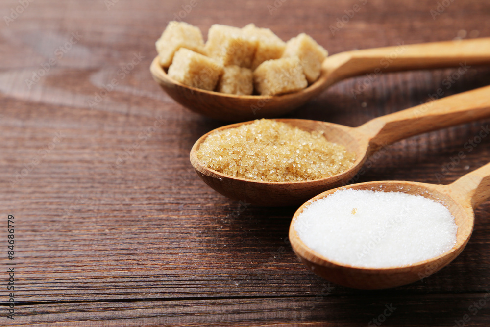 Various kinds of sugar in spoons on brown wooden background