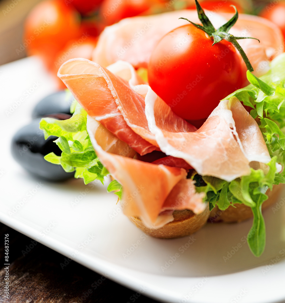 thin slices of prosciutto with olives and tomato on plate