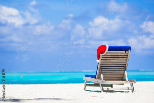 Fototapeta Naklejka Na Ścianę i Meble -  Sun chair lounge with red Santa Hat on tropical white beach and