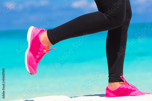 Close-up of female legs in sneakers running on white sandy beach © travnikovstudio