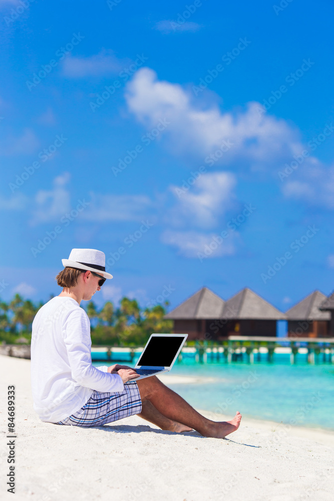 Young man working on laptop at tropical beach near water villa