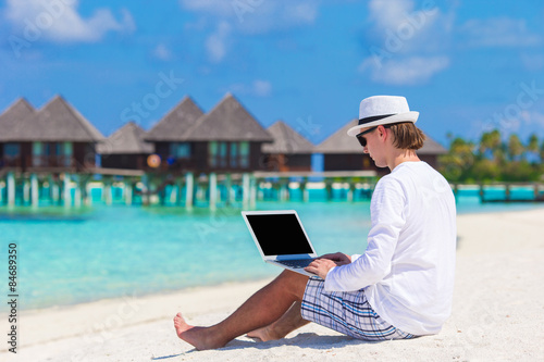 Young man working on laptop at tropical beach near water villa © travnikovstudio