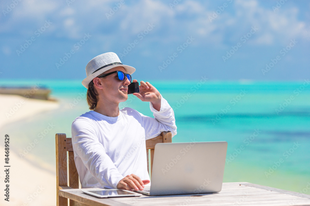 Young businessman with computer and cell phone on white beach