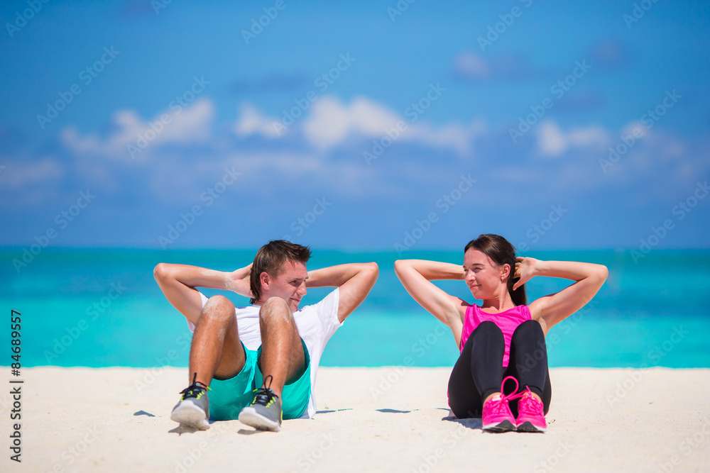 Young fitness couple doing sit ups on white beach Young fitness couple doing sit ups on white beach