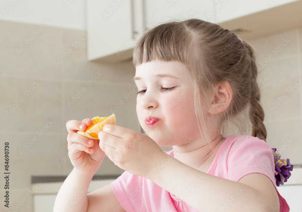 Happy little girl eating a tasty orange