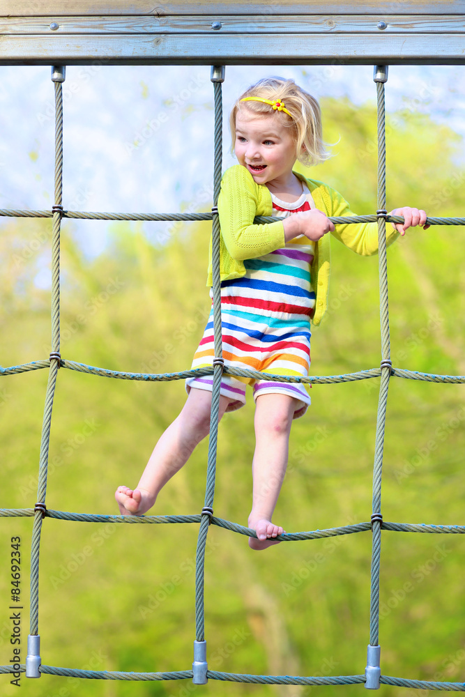 Adorable happy little child, blond sportive toddler girl, having fun outdoors climbing on playground in the park on a sunny spring or summer day