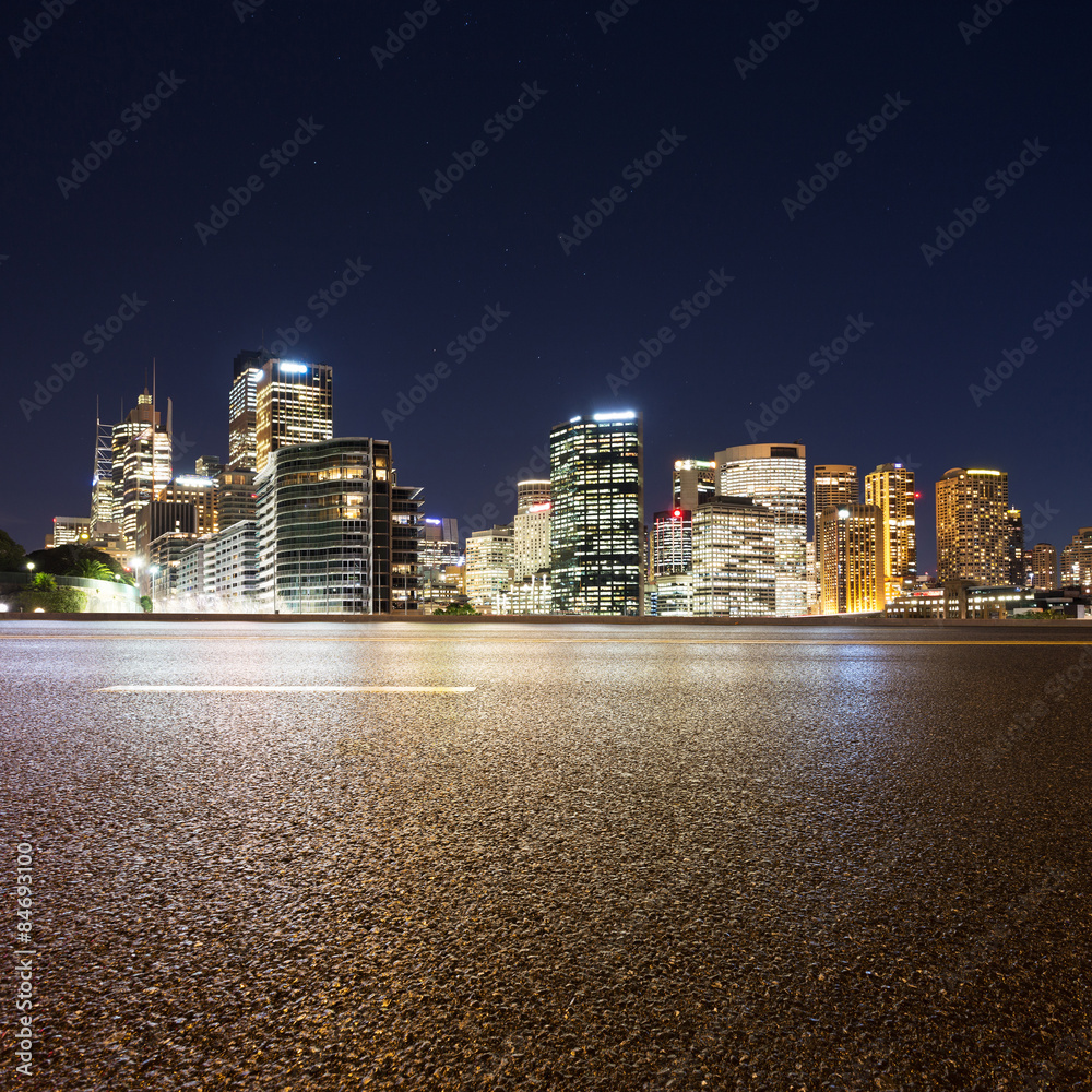 Fototapeta premium Empty asphalt road and illuminated modern cityscape background a