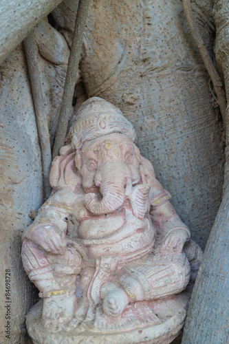 Statue of Hindu God Ganesha sitting in the root of tree