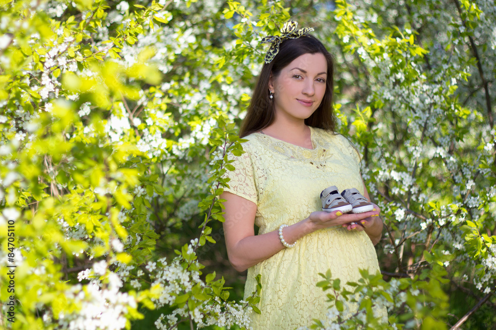 pregnant woman holding little shoes in blooming cherry garden pregnant woman holding little shoes in blooming cherry garden