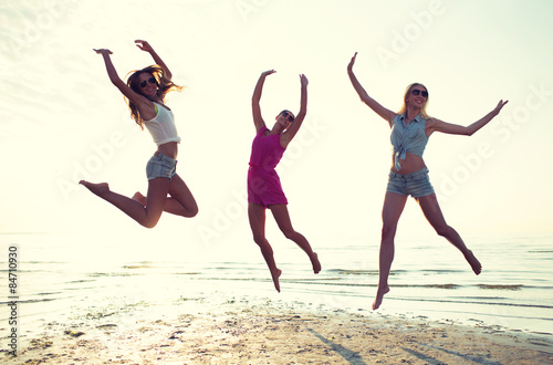 happy female friends dancing and jumping on beach