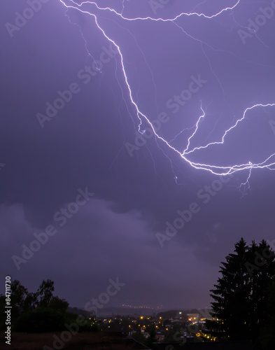 Lightnings over a city in blue sky with a tree 