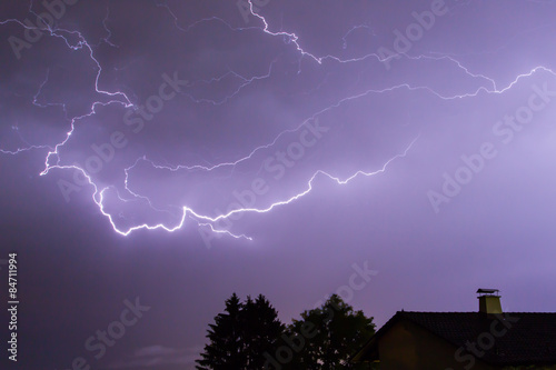 Lightnings in blue sky with a house and a tree