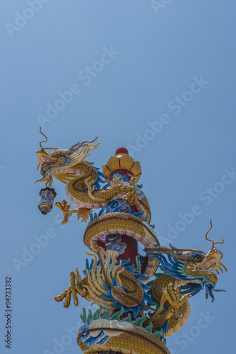 Colorful two dragons statue on pole with blue sky background.