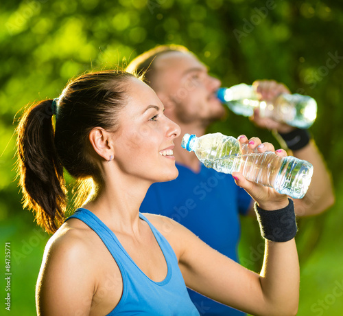 Man and woman drinking water from bottle after fitness sport