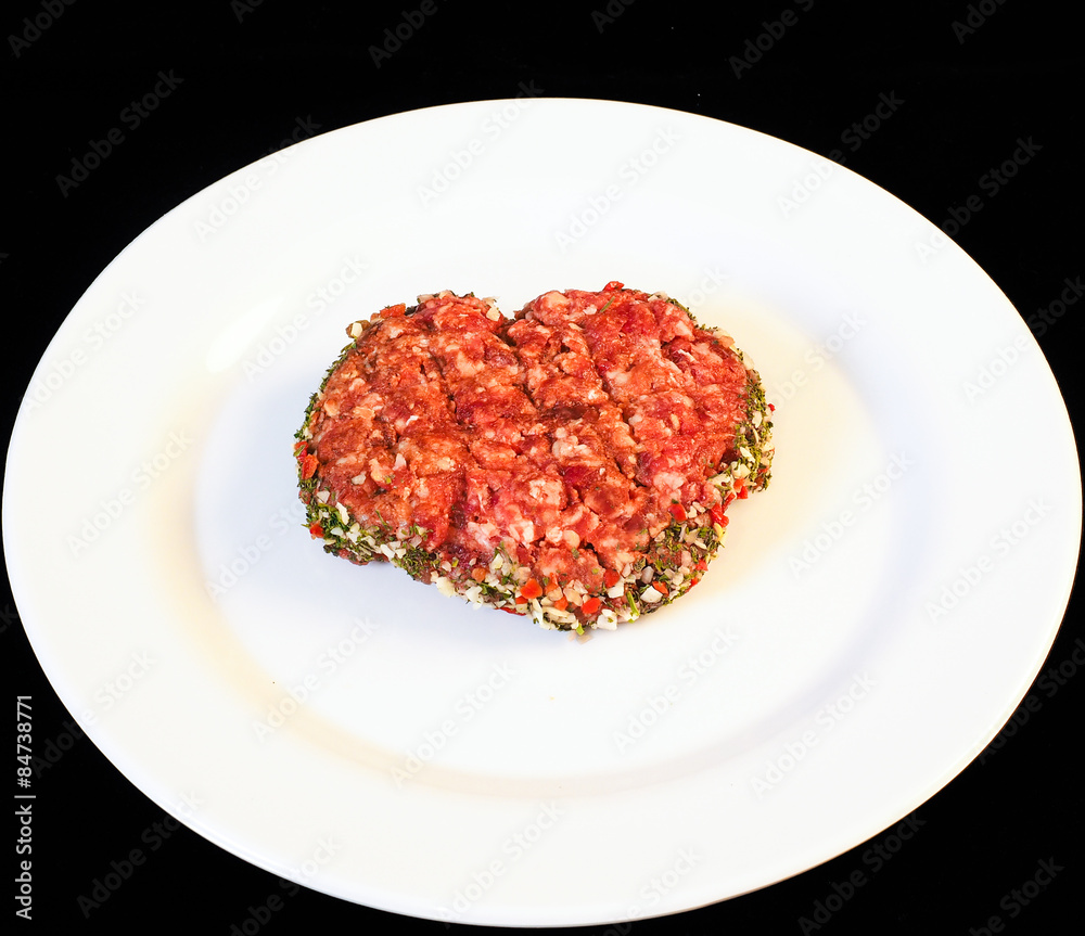Seasoned raw red hamburger on white plate isolated on black