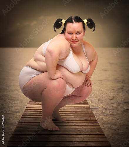 Overweight woman in bikini posing on a pier over sea.  photo