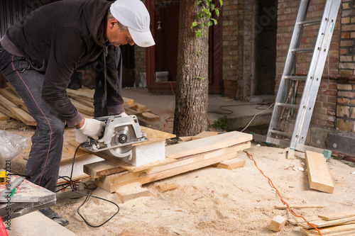 Man Using Power Saw to Cut Planks of Wood