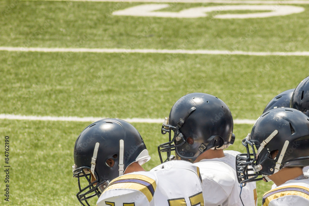 Fototapeta premium Kids standing on a football field with black helmets and white jerseys 