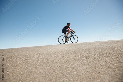 Male cyclist riding on a flat road against blue sky