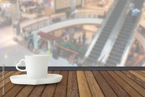 Coffee cup on wood table with fade out of shopping mall as backg