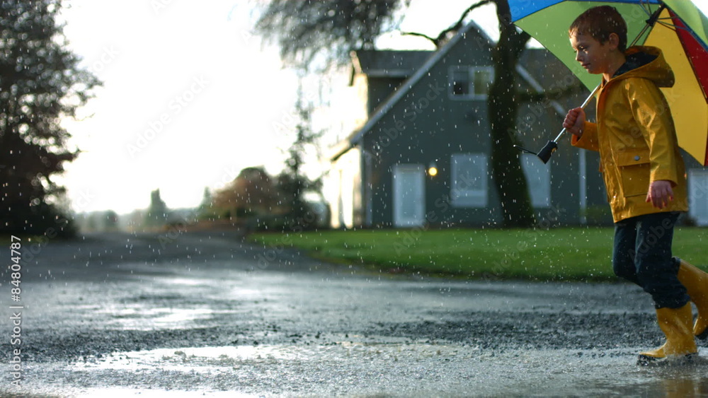 Young boy running through puddles with umbrella, slow motion
