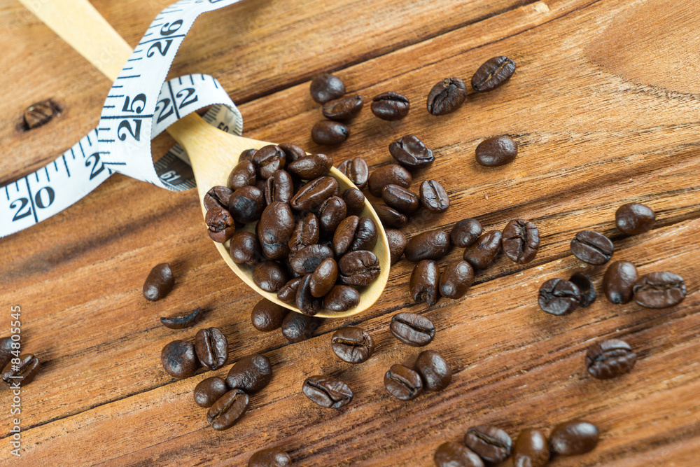 Coffee bean on wooden spoon, tape measure on wooden background Coffee bean on wooden spoon, tape measure on wooden background