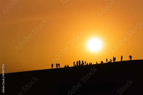Peoples watching the sunset - silhouettes of people on dune looking on orange sun in desert