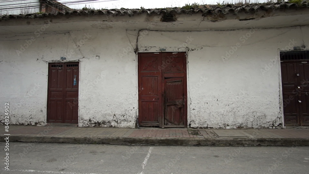 Panning shot of an old dilapidated adobe style colonial era building situated on a modern day asphalt street.