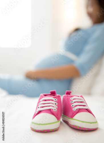 A pair of pink toddler sneakers beside a pregnant woman, focus o