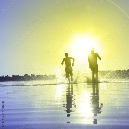 Gl  ckliche junge Menschen laufen und springen am See beim Sonnenuntergang